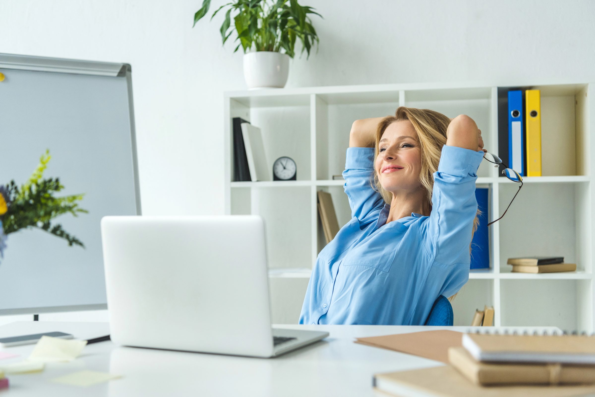 Business owner leaning back at her desk, relaxed and smiling in a bright office