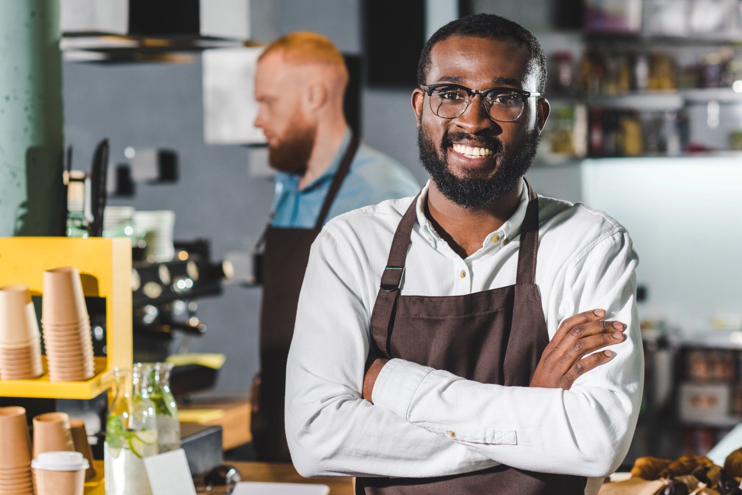 Caf&eacute; owner smiling with arms crossed at the counter of his shop